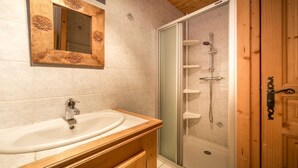 A bathroom with a wooden vanity, a sink, a mirror, and a glass-enclosed shower area. - Sermes 1 - Spacious apartment in the centre (MORZINE)
