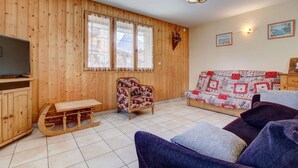 A wooden-paneled room with a sofa, a patterned armchair, a wooden table, and a television. - Sermes 1 - Spacious apartment in the centre (MORZINE)
