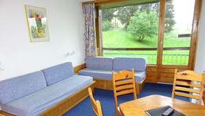 A room with a blue sofa, wooden chairs, a small table, and a window with a view of a green landscape. - Ski-in studio for 5, pets allowed at Arc 1800 (Les Arcs 1800)