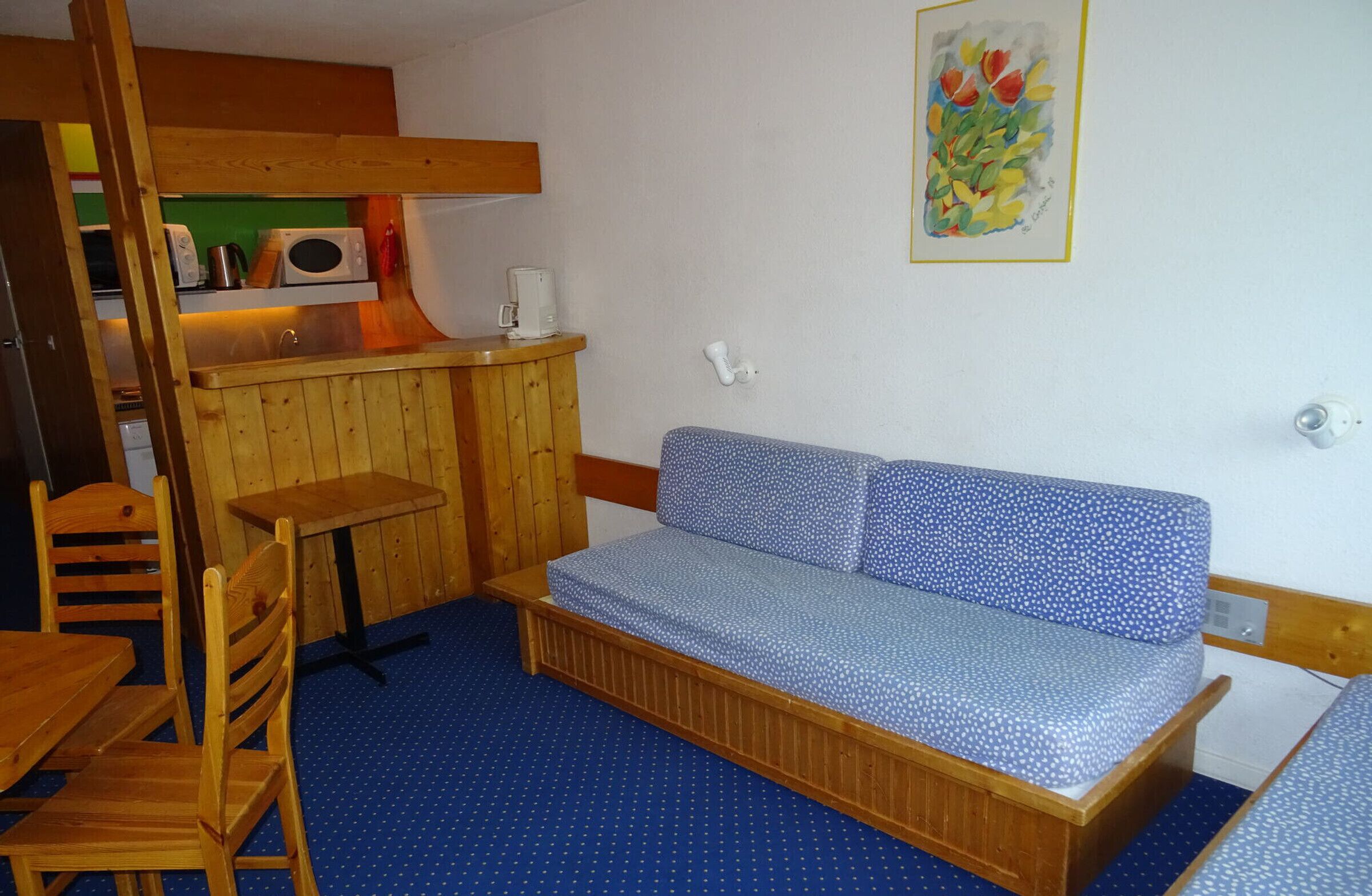 A small, cozy room with a wooden bench, a small table, and a kitchenette area.