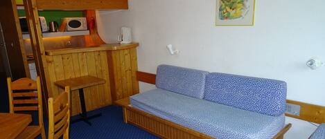 A small, cozy room with a wooden bench, a small table, and a kitchenette area.