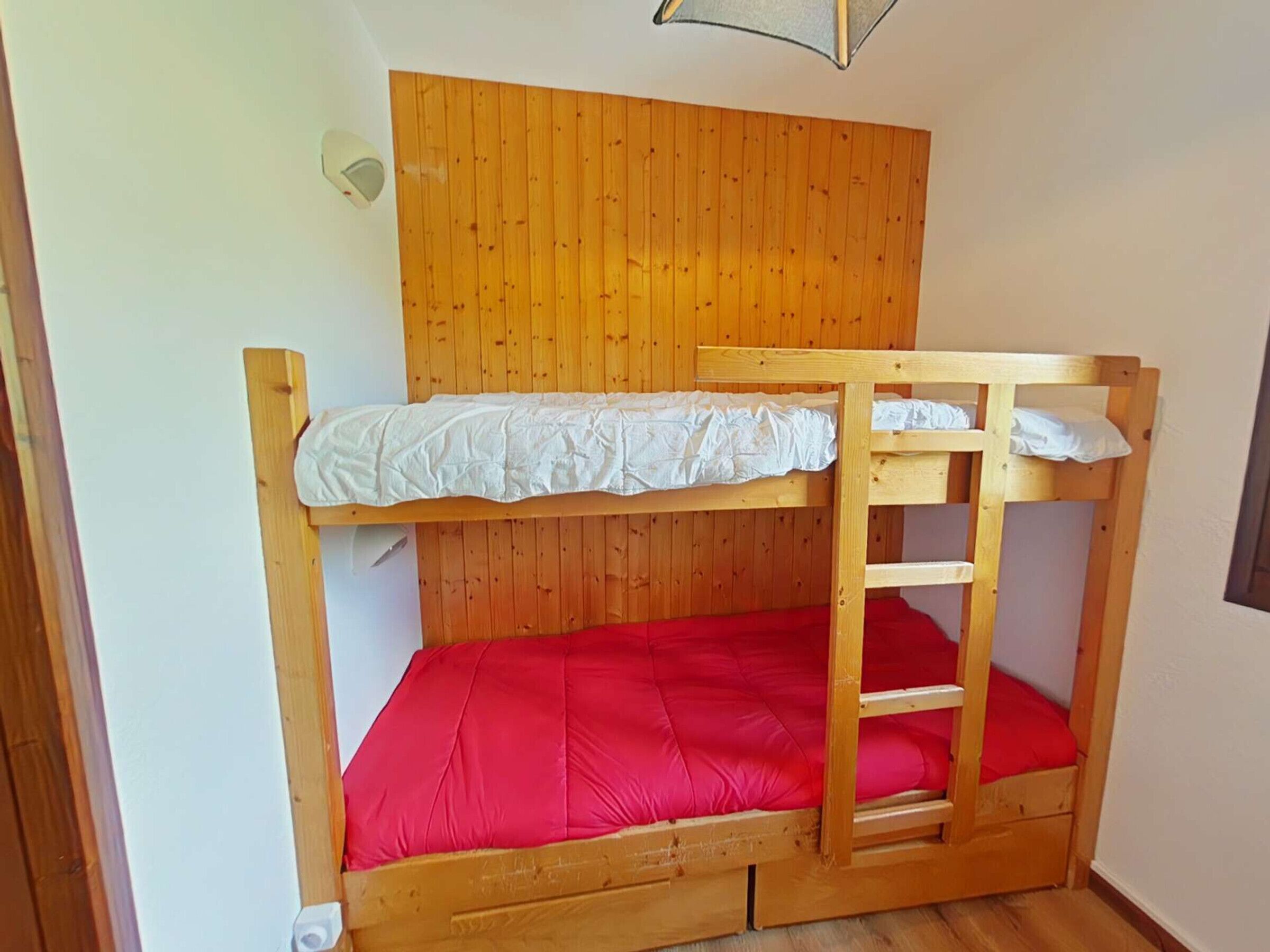 Een stapelbed met een houten hoofdbord en een rode matras.