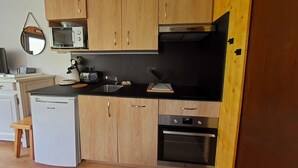 Een kleine keuken met houten kastjes, een inbouwmagnetron, een broodrooster, een spoelbak en een vaatwasser.