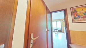 Een houten deur met een moderne hendel, die leidt naar een kamer met een balkon en een schilderij aan de muur.