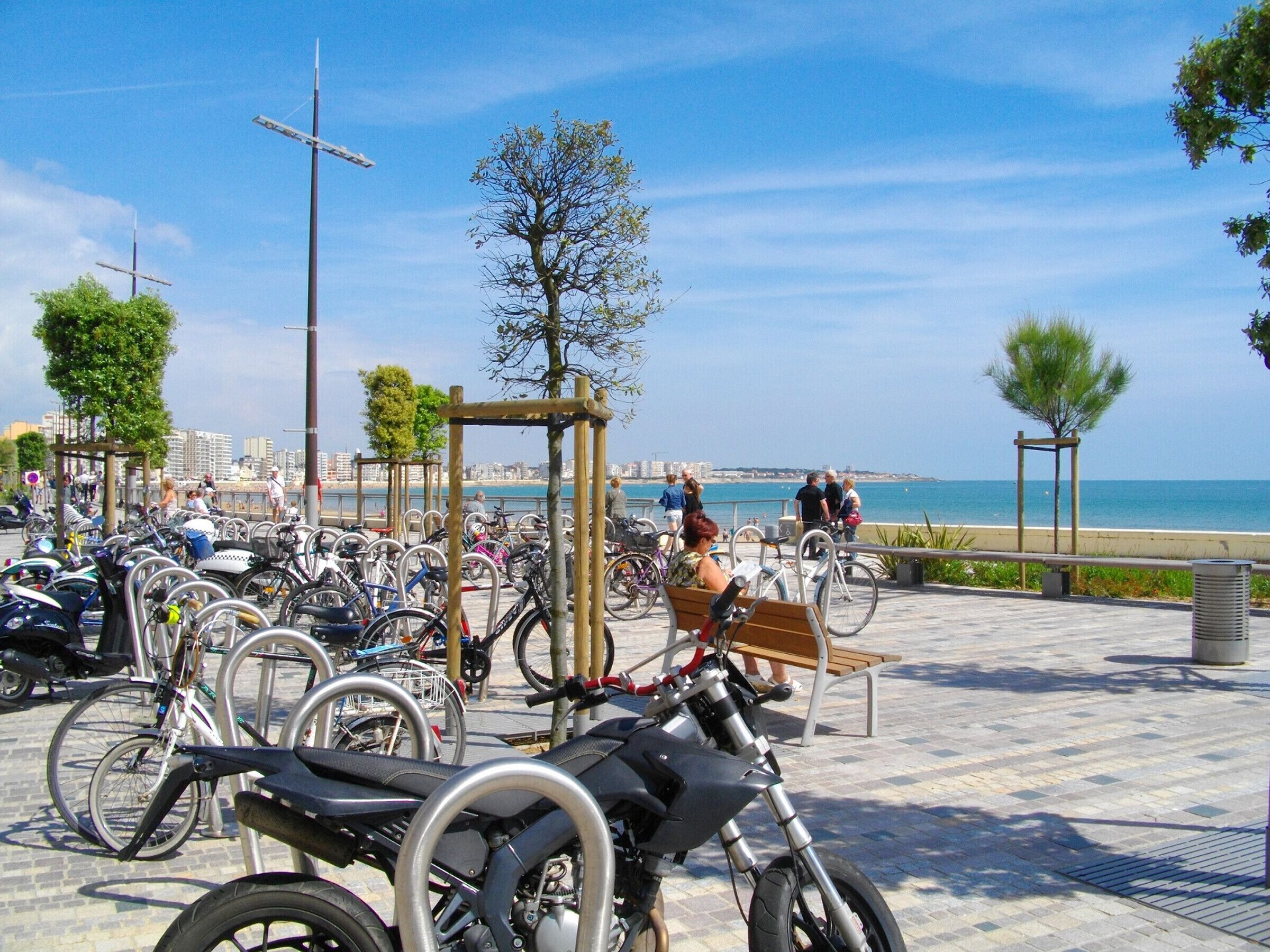 A paved area with bicycles and a bench, overlooking a body of water and buildings in the distance.