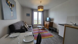 Un salon moderne avec un canapé, une table à manger dressée avec des assiettes et des verres, un téléviseur posé sur un meuble en bois et un tapis coloré.