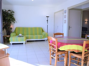 Una sala de estar con un sofá, una mesa de comedor con sillas, una lámpara de pie y una planta en maceta.