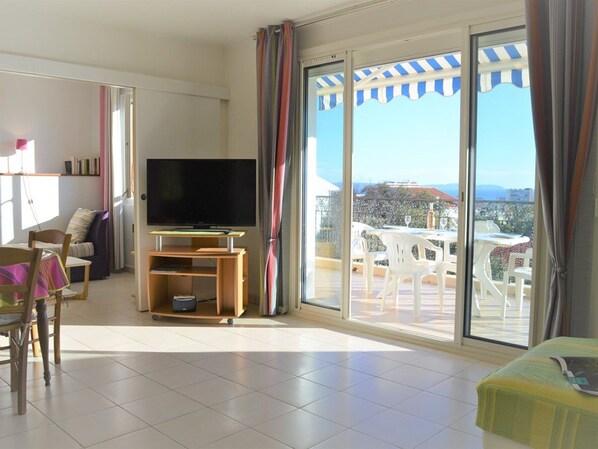 Un vaste espace de vie doté d’un téléviseur à écran plat, d’une table à manger avec des chaises et d’un balcon avec des sièges d’extérieur.