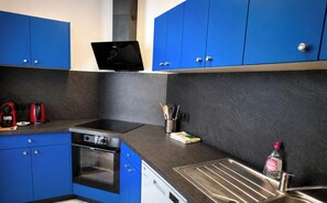 A modern kitchen with blue cabinets, a black stove, a coffee maker, and a sink.