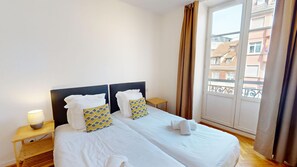 A hotel room with a double bed, two bedside tables, a lamp, and a view of buildings through a window. - netter 70m2 city center    2br (Strasbourg)