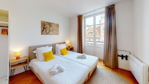 A hotel room with a double bed, a bedside table with a lamp, a window with curtains, and a radiator. - netter 70m2 city center    2br (Strasbourg)