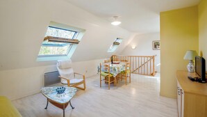 A spacious loft bedroom with a high ceiling, skylights, a dining area with a table and chairs, a bed, and a small desk with a lamp. - Homerez - Comfort apt Arzon (Arzon)
