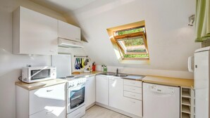 A compact kitchen with white cabinets, a microwave, an oven, a dishwasher, and a window with a view of greenery. - Homerez - Comfort apt Arzon (Arzon)