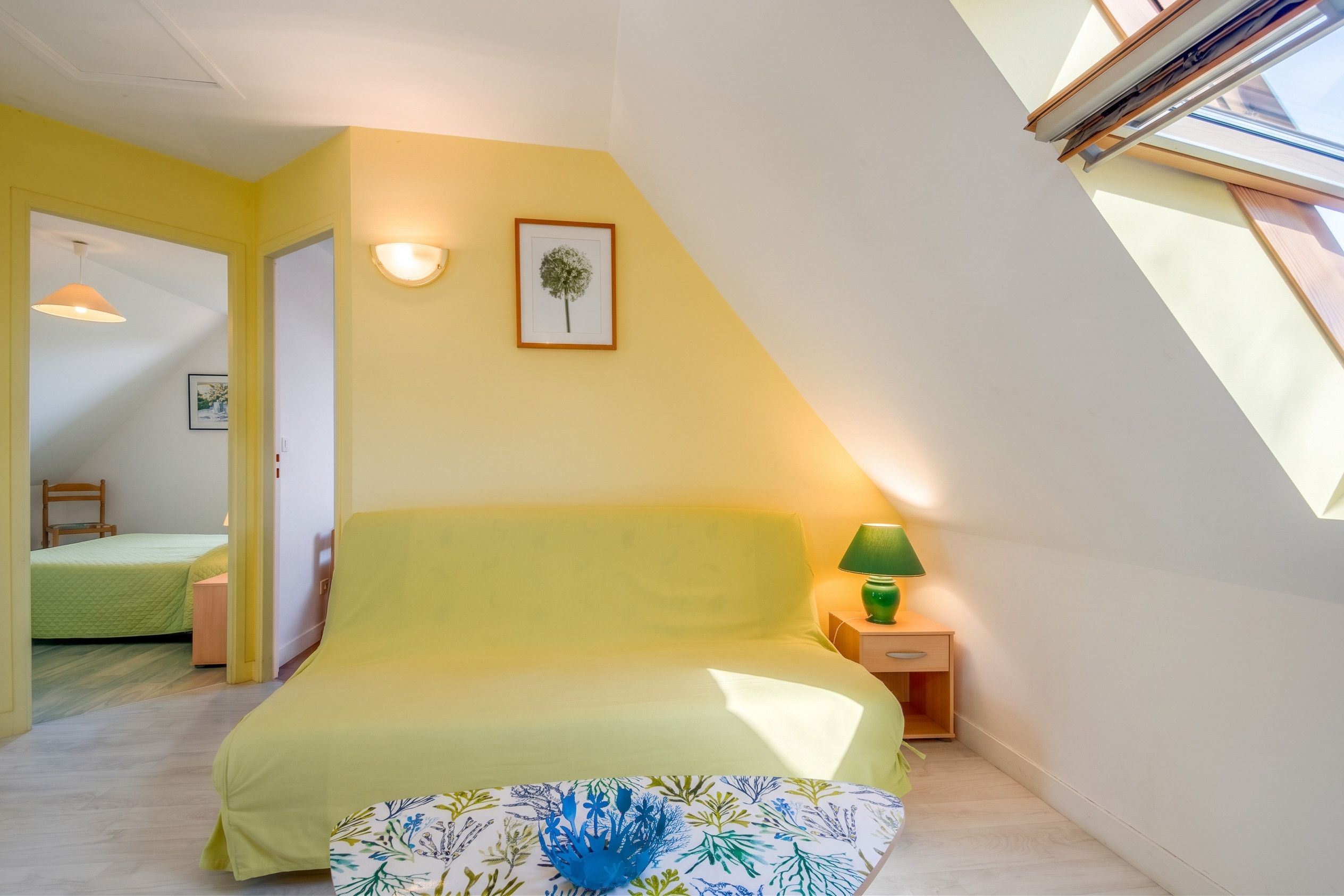 Une chambre à coucher avec un lit, une table de chevet, une lampe, un tableau encadré au mur et une lucarne.