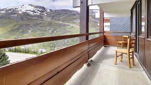 A balcony with a wooden railing, a wooden bench, and a view of a mountain range. - Spacious ski-in/ski-out apartment with balcony (Les Menuires)