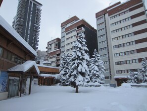 Un cortile innevato con un edificio a più piani e balconi, circondato da alberi carichi di neve.