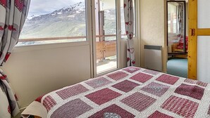 A bedroom with a large window, a bed with a patterned bedspread, and a view of a mountain. - Spacious ski-in/ski-out apartment with balcony (Les Menuires)