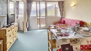 A cozy room with a dining table set for two, a sofa, a TV, and a view of the mountains. - Spacious ski-in/ski-out apartment with balcony (Les Menuires)