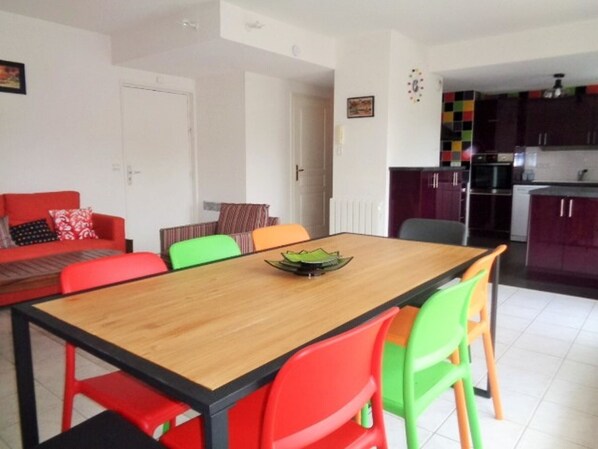 A dining area with a wooden table and colorful chairs, a red sofa, and a kitchen in the background. - **Modern Duplex in Arcachon: Terrace, WiFi, Parking, 150m from Beach** (Arcachon)