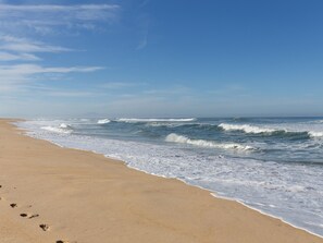 A beach with waves, a clear sky, and footprints in the sand.