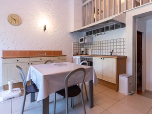 A compact kitchen with a dining table, chairs, a microwave, and a clock on the wall.
