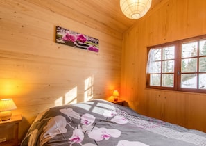 A wooden room with a bed, a window, and a wall-mounted picture.