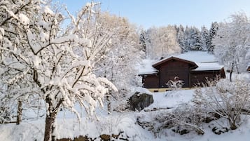 A wooden cabin surrounded by snow-covered trees and rocks.