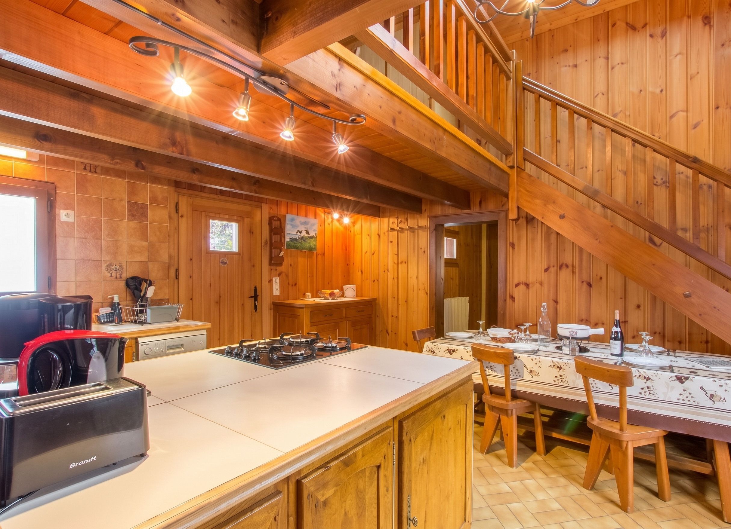 A wooden interior with a kitchen area, dining table, and a staircase.