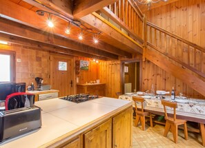A wooden interior with a kitchen area, dining table, and a staircase.