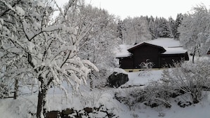 A snow-covered landscape with a wooden cabin surrounded by trees.