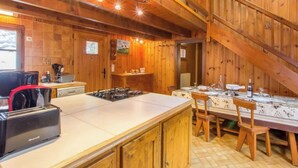 A rustic kitchen with a wooden interior, a gas stove, a sink, and a dining area with a table set for four.