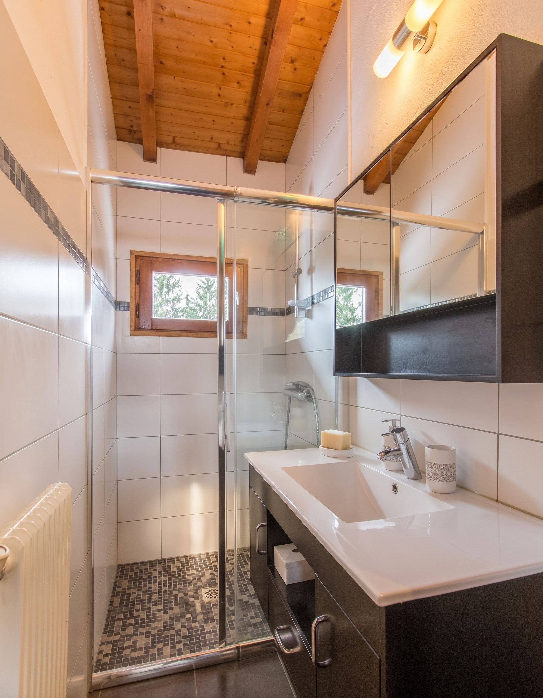 A modern bathroom with a glass shower enclosure, a white sink, and a large mirror.