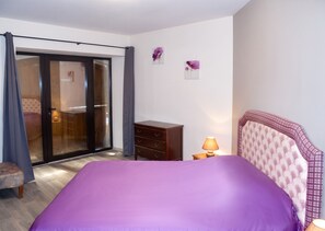 Une chambre à coucher comprenant un lit, une commode, une table de chevet, une lampe et une porte-fenêtre coulissante.