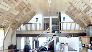 Ein geräumiger Loft mit hoher Decke, freiliegenden Holzbalken, einer zentralen Treppe, einer Küchenzeile und einem Essbereich.