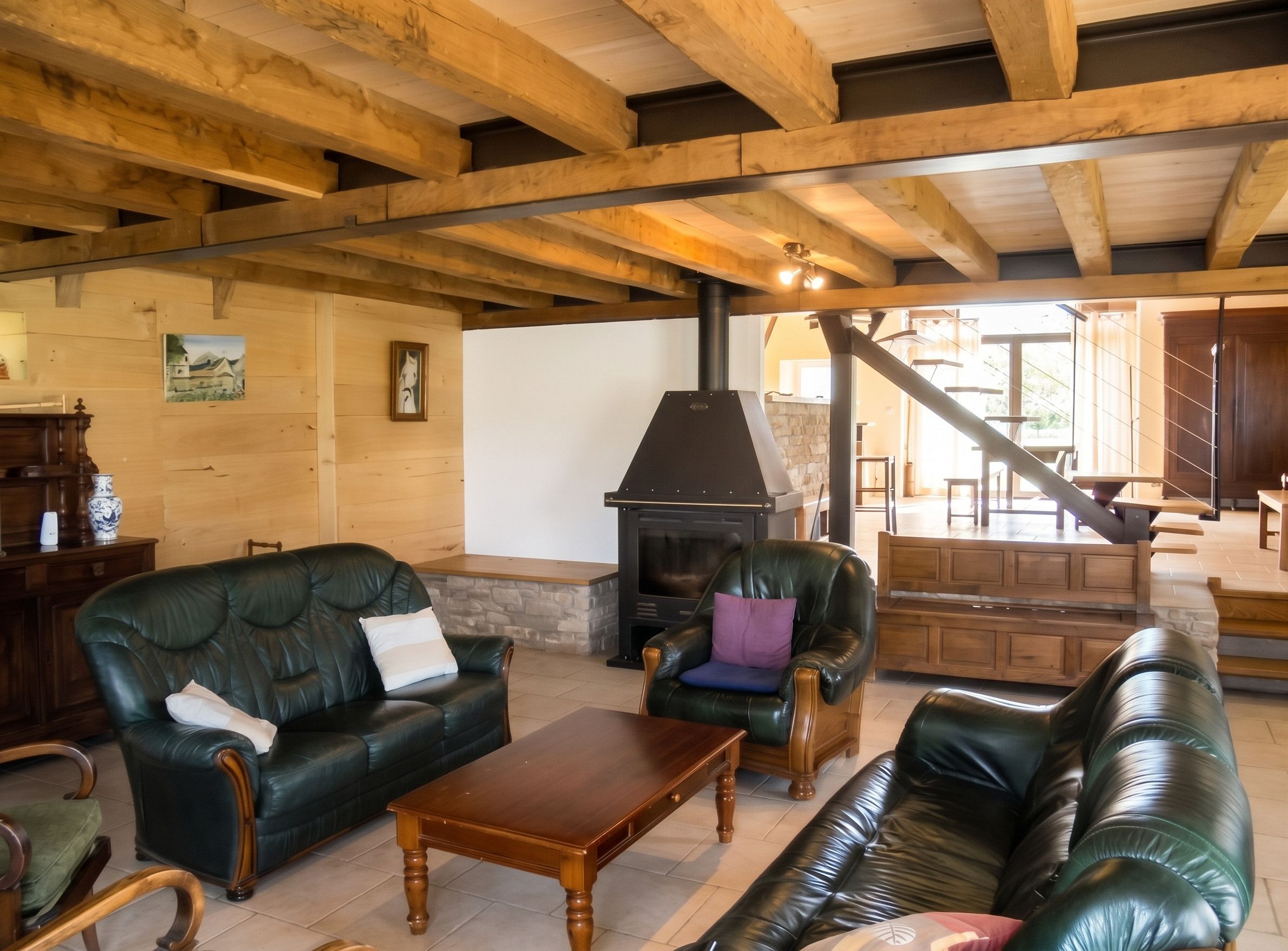 A spacious living room with a fireplace, leather sofas, and a wooden ceiling.