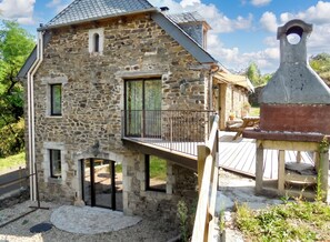 Una casa de piedra con balcón, chimenea y una parrilla pequeña al aire libre.