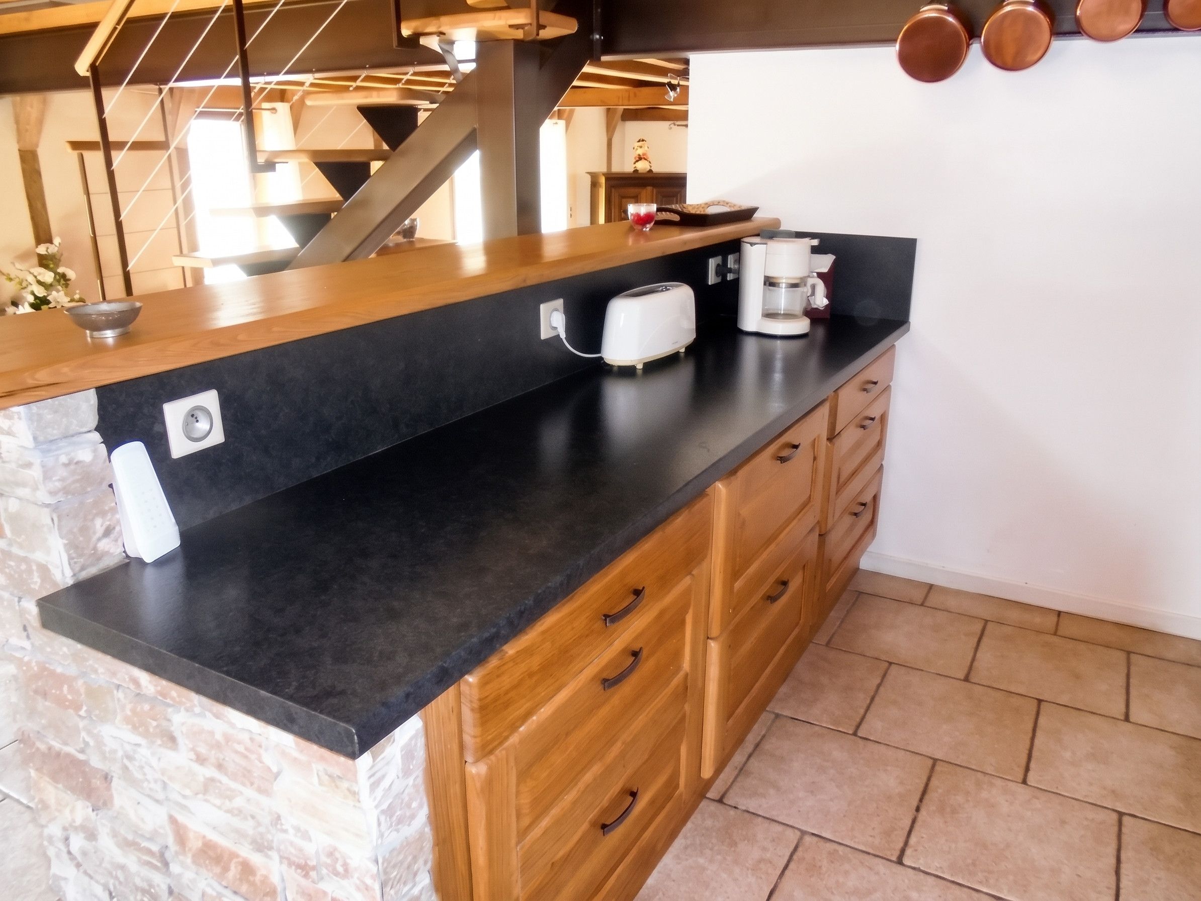 A kitchen with a black countertop, wooden cabinets, a coffee maker, and a toaster.