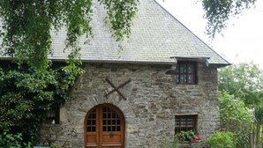 A stone cottage with a wooden door, a small window, and a garden with a table and chairs.