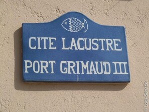 Une enseigne portant l'inscription « CITE LACUSTRE PORT GRIMAUD III » et surmontée d'un symbole de poisson.