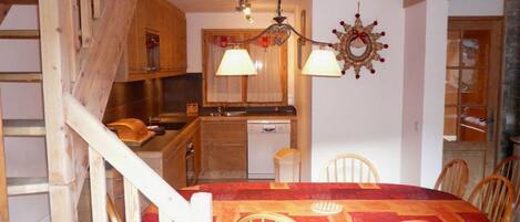 A rustic kitchen with wooden cabinets, a dining table with chairs, and a chandelier.