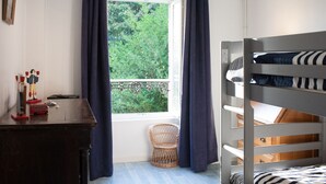 Ein Schlafraum mit Etagenbetten, einem Fenster, einem Schreibtisch mit Spielzeug und einem Korbstuhl.