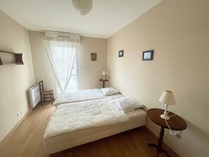 Une chambre avec deux lits, une chaise, une table avec une lampe et un radiateur.