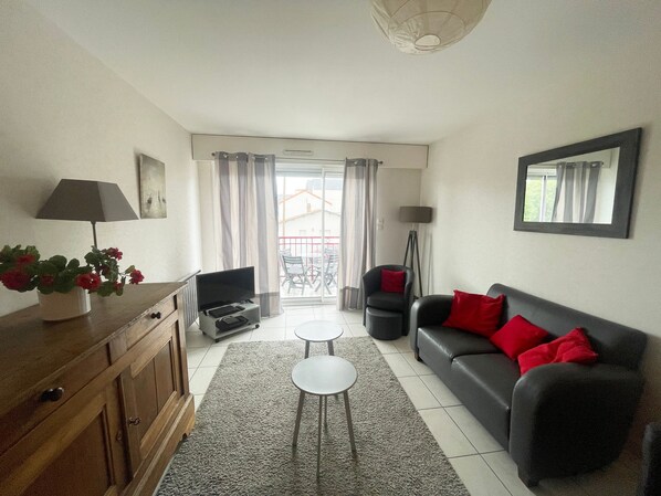 Un salon avec un canapé, un téléviseur, une petite table, une lampe et une plante en pot.