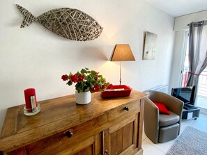 Een woonkamer met een houten kast, een rode kaars, een bloempot met rode bloemen, een lamp en een vis decoratie aan de muur.