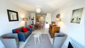A living room with a sofa, armchairs, a coffee table, a dining table, and a TV. - Elegant Apartment with Garage – 400m from Beach (Les Sables-d'Olonne)