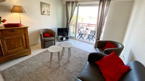 A living room with a sofa, two armchairs, a TV, a wooden cabinet, and a balcony with outdoor furniture. - Elegant Apartment with Garage – 400m from Beach (Les Sables-d'Olonne)