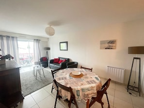 Un comedor con una mesa dispuesta para cuatro personas, un sofá con cojines rojos, una lámpara de pie y un cuadro en la pared.