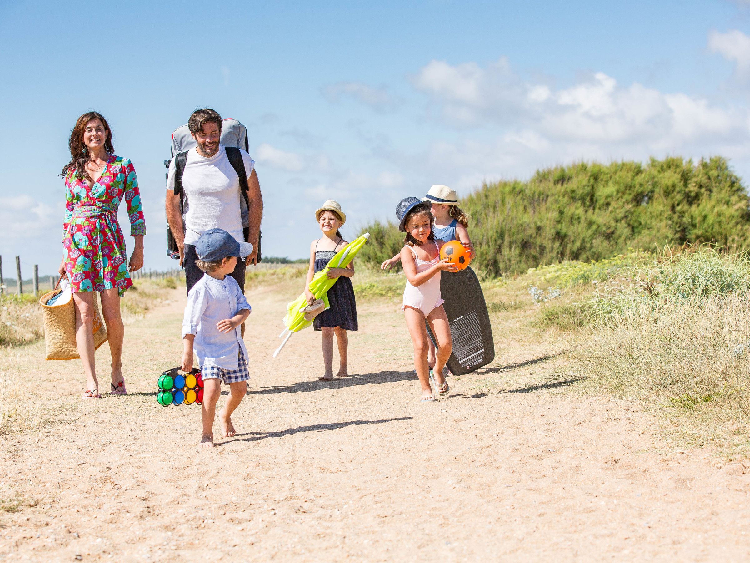 Eine Familie geht auf einem Feldweg, im Hintergrund ist ein Strand zu sehen.