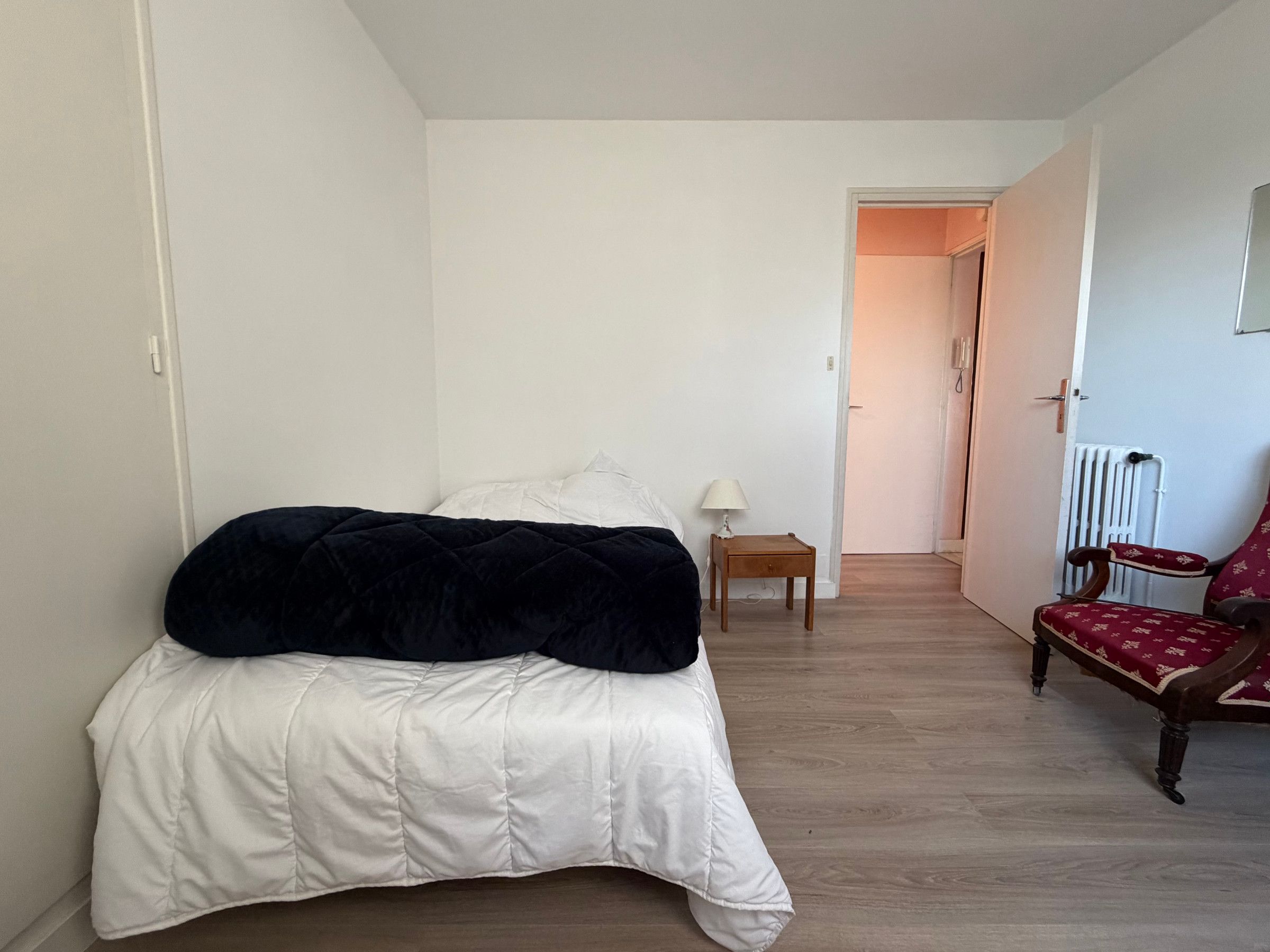 Een slaapkamer met een bed, nachtkastje, stoel en radiator.