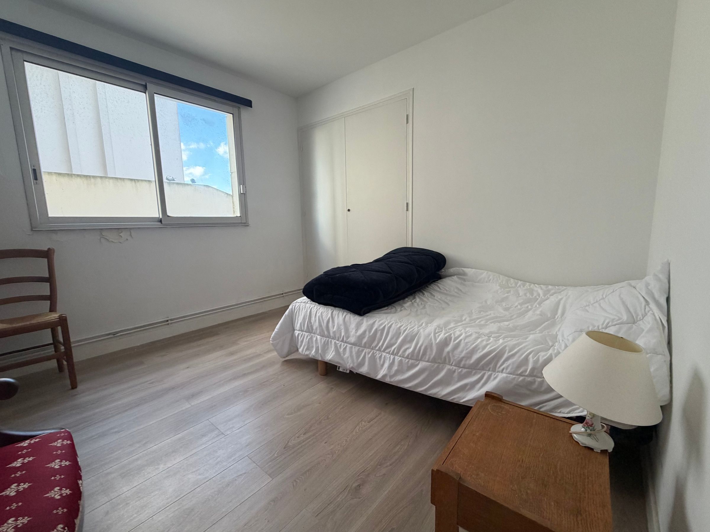 Ein Schlafzimmer mit einem Bett, einem Sessel, einem Nachttisch mit Lampe und einem Fenster.